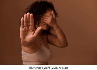 A Dark-haired Curly Young Woman In Beige Underwear Covers Her Face And Shows A STOP Sign With Her Hand. Concept Of Body Positive, Self-confidence And Ending Violence And Oppression Against Women