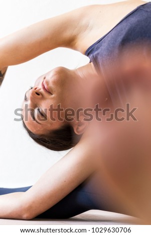 A dark-haired European woman concentrated on a revolved Head-of-Knee Pose or Parivrtta Janu Sirsasana, vertical view.