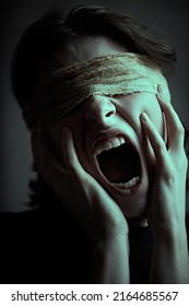 A Dark-haired Girl With Bandaged Eyes Holds Her Face With Her Hands And Screams In Severe Pain. Human Suffering, Blindness.