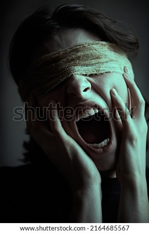 A dark-haired girl with bandaged eyes holds her face with her hands and screams in severe pain. Human suffering, blindness.