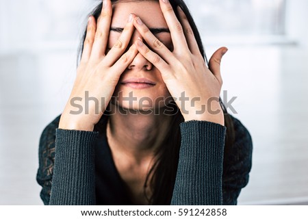 Dark-haired girl covers her face with hands
