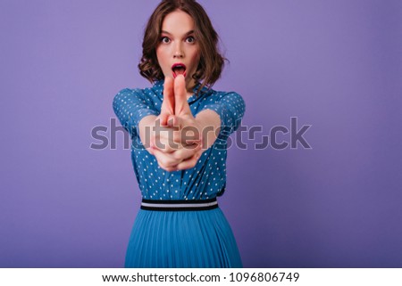 Dark-haired girl wears blouse and skirt funny posing on purple background. Indoor shot of carefree curly female model playing during photoshoot.