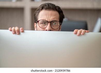 A dark-haired man hiding behind the computer and looking stressed