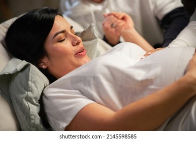 Dark-haired woman giving birth at home. Woman with pierced nose lying, feeling contractions during childbirth. Pregnancy, home birth concept - Shutterstock ID 2145598585