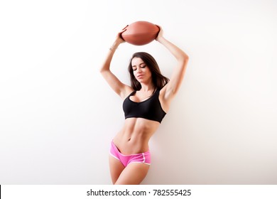 Dark-haired young woman fitness model holds a  rugby ball over his head 
 and seductively posing on white isolated background - Powered by Shutterstock