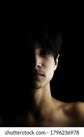 Darkness. Horror. Portrait Of A Guy On A Black Background. Asian Teenager. One Light Source. Half Face In Shadow. Black Background. Portrait Of An Unusually Handsome Guy