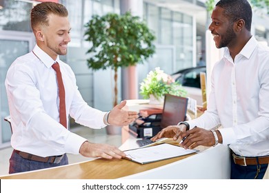 Dark-skinned Afro Clients And Confident Caucasian Manager Or Consultant Are Talking In Car Showroom, Client Going To Buy New Representative Business Class Auto In Dealership