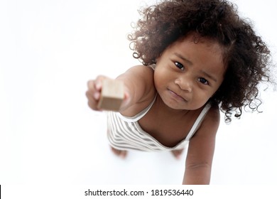 Dark-skinned girl stretches her hand to the camera with a serious expression, hand the wooden block, top view, white background, selective focus