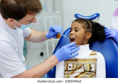 Dark-skinned Little Girl Sitting In A Blue Dental Chair At A Reception At The Dentist