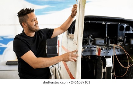 A dark-skinned man in his 30s and 40s is fixing a small plane at an aircraft shop. The Latin technician is fixing the door of the light plane. Concept of Dominican technicians or engineers. - Powered by Shutterstock