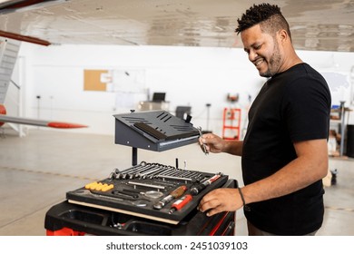 A dark-skinned man in his 30s and 40s is fixing a small plane at an aircraft shop. The Latin technician is choosing the right tool for the arrangements. Concept of Dominican technicians or engineers - Powered by Shutterstock
