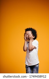 A Dark-skinned Maracan Boy In A White T-shirt Closed His Eyes With His Hands To Start The Game Of Hide And Seek On An Orange Background