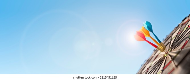 Dart in bulls eye of dartboard with blue sky background concept for hitting target, goal and success - Shutterstock ID 2115451625