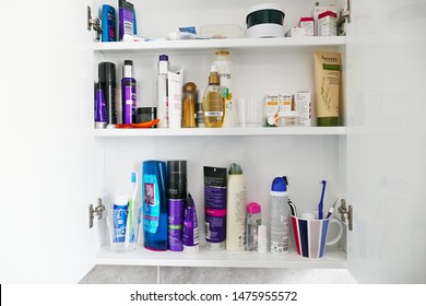 Dartmoor England. Inside of a domestic bathroom cabinet showing tubs of cosmetics, toothpaste, skincare, and brushes, hair shampoo. In cupboard with three shelves. Beauty products