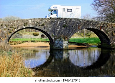 Dartmoor England. Motorhome passing over Two Bridges an ancient stone bridge with double arch. Reflection in river. Green river bank. Blue cloud. 