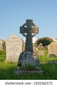 Dartmouth, Devon UK 30 June 2021 : Celtic Cross Gravestone In The Grass With Blue Background. Sun And Shadow On Graves At Cemetery