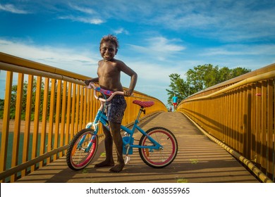 DARWIN, AUSTRALIA- MARCH 14, 2017: Australian Aboriginal Boy Enjoys The Evening Of Summer Hanging Around On Cycle In The Bridge Of Rapid Creek In Darwin, NT. He Likes To Ride A Cycle In This Outback.