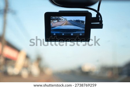 Dash camera mounted on car windshield recording urban traffic with blurred road background, symbolizing driving safety, technology, surveillance, transportation, and modern travel lifestyle.