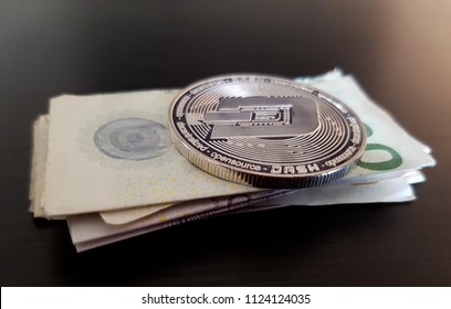 Dash physical cryptocurrency coin lying on a stack of money. The currency is danish danske kroner. Background is dark themed with light from above