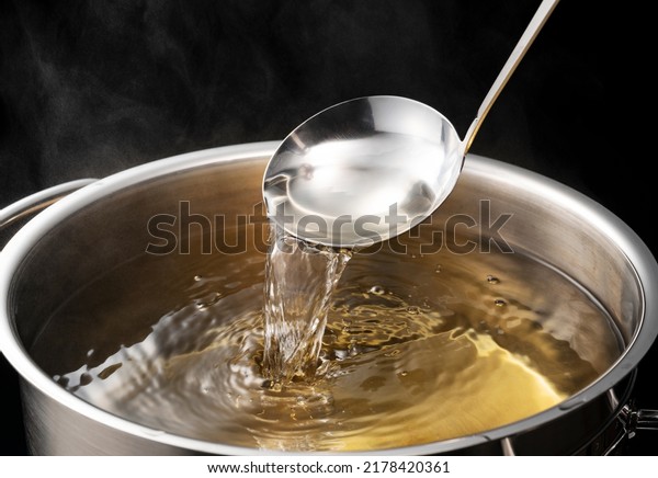 Dashi, soup stock, and the\
basics of Japanese cuisine. Black background. Steam. Scooping with\
a ladle.
