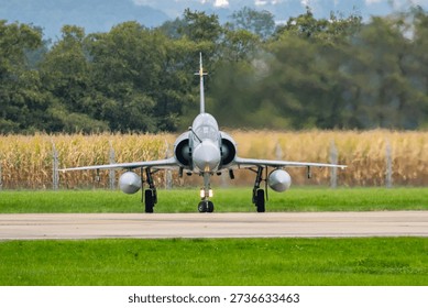 Dassault Mirage 2000 preparing for takeoff at an airfield with greenery and crops in the background