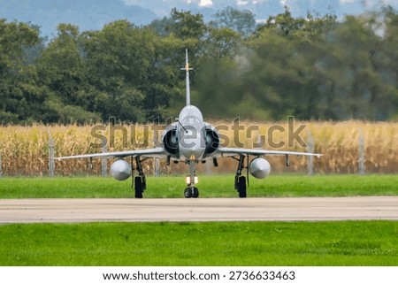Dassault Mirage 2000 preparing for takeoff at an airfield with greenery and crops in the background