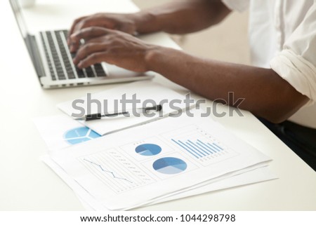 Data analysis and business statistics concept, african-american businessman using laptop analyzing work result infographic stats graphs and charts, making report or strategic planning, close up view