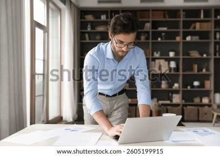 Data analyst at work. Serious young businessman project manager student use digital tools paper documents at workplace to create finance report academic research browse web on notebook to review data
