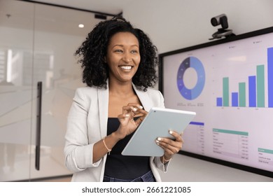Data analyst at work. Successful smiling young Black businesswoman pose in innovative office use digital tools tablet interactive screen to develop insights ideas strategies of future business growth