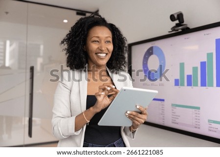 Data analyst at work. Successful smiling young Black businesswoman pose in innovative office use digital tools tablet interactive screen to develop insights ideas strategies of future business growth