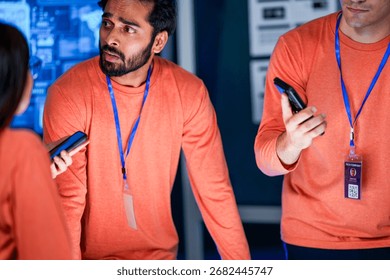 A data analytics team in a command center reviews a live security feed on a mobile device. They are collaborating on a strategy to respond to a new threat on the network.