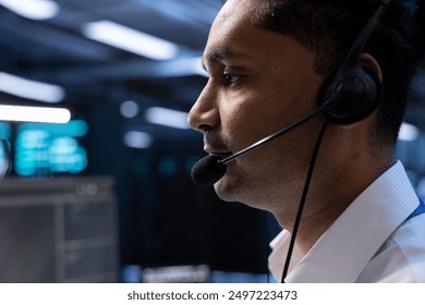 Data center agent assisting engineering teams with hardware installations, issuing commands though headset mic. Close up of IT specialist in server farm communicating with engineers in remote call