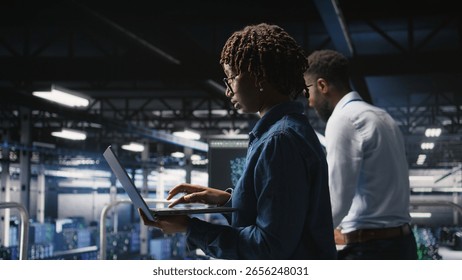 Data center computer scientist doing maintenance tasks on laptop, ensuring optimal performance. African american technician reviewing diagnostics and applying patches to server hub gear,