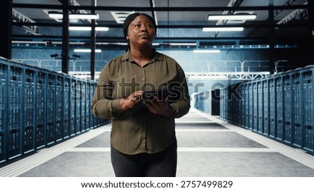 Data center employee using tablet to manage software updates for system stability. African american engineer in server room configuring infrastructure with device for optimum performance, camera A
