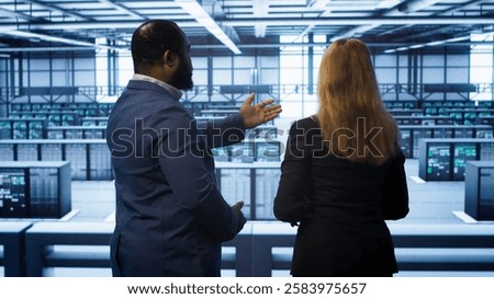 Data center engineer presenting equipment to inspector supervising operations. IT specialist in server farm doing tour for supervisor monitoring equipment performance, camera A