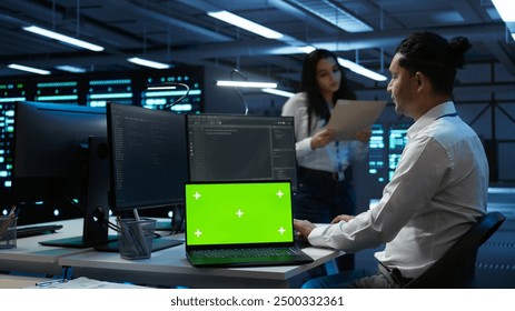 Data center engineer responsible for installation of networking equipment solving tasks on isolated screen laptop. Man doing maintenance on server room infrastructure using mockup notebook, camera B