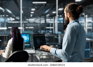 Data center engineer working on databases supporting AI apps using laptop. IT employee in server room using artificial intelligence technology to do algorithms improvements