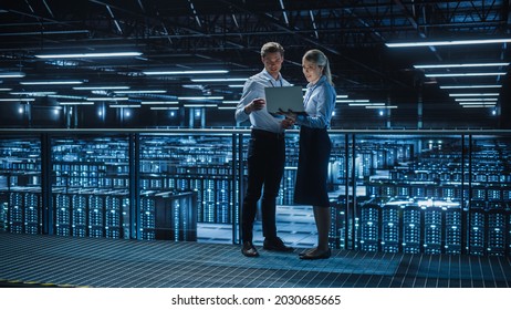 Data Center Female e-Business Enrepreneur and Male IT Specialist talk, Use Laptop. Two Information Technology Engineers on Bridge Overlooking Big Cloud Computing Server Farm. - Shutterstock ID 2030685665