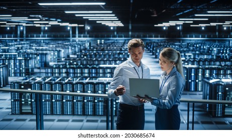 Data Center Female e-Business Enrepreneur and Male IT Specialist talk, Use Laptop. Two Information Technology Professionals on Bridge Overlooking Big Cloud Computing Server Farm.