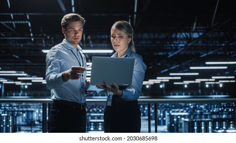 Data Center Female e-Business Enrepreneur and Male IT Specialist talk, Use Laptop. Two Information Technology Professionals on Bridge Overlooking Big Cloud Computing Server Farm. - Shutterstock ID 2030685698