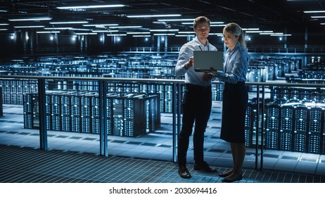 Data Center Female e-Business Enrepreneur and Male IT Specialist talk, Use Laptop. Two Information Technology Engineers work on Bridge Big Cloud Computing Server Farm.
