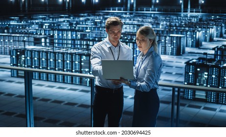 Data Center Female e-Business Enrepreneur and Male IT Specialist talk, Use Laptop. Two Information Technology Engineers work on Bridge Big Cloud Computing Server Farm.