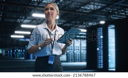 Data Center Female e-Business Entrepreneur Use Tablet Computer with Pleasure Smile. Information Technology Engineer and System Administrator work in Big Cloud Computing Server Farm.