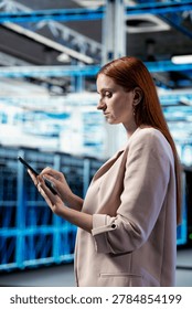 Data center female engineer using tablet app to evaluate equipment diagnostic reports. Woman in server hub scripting automated workflows using touchscreen device to oversee mainframes