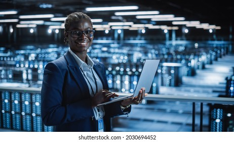 Data Center: Female Programmer Using Laptop Computer, Smiling and Looking at Camera. In Cloud Computing Server Farm System Administrator Working on IT Maintenance for Iaas, saas, paas. - Powered by Shutterstock