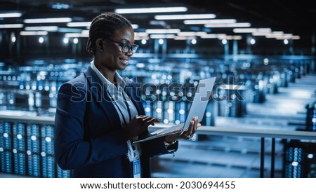 Data Center Female Programmer Using Laptop Computer, Maintenance IT Specialist. In Cloud Computing Server Farm Smiling System Administrator Working on Cyber Security for Iaas, saas, paas.