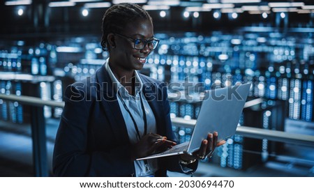Data Center Female Programmer Using Laptop Computer, Maintenance IT Specialist. In Cloud Computing Server Farm Smiling System Administrator Working on Cyber Security for Iaas, saas, paas.