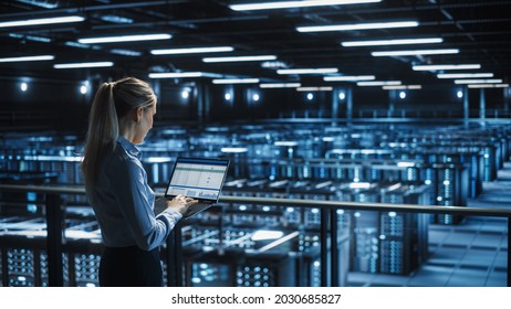 Data Center Female IT Specialist Uses Laptop Computer. Cloud Computing Server Farm With IT Engineer Monitoring Statistic, Maintenance Control. Information Technology Of Fintech, E-Business.