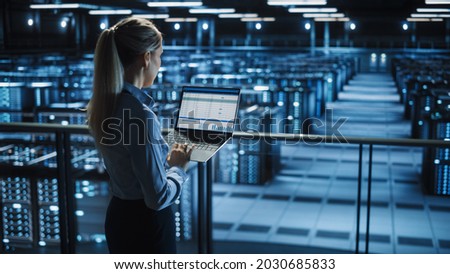 Data Center Female IT Specialist Uses Laptop Computer. Cloud Computing Server Farm with IT Engineer Monitoring Statistic, Maintenance Control. Information Technology of Fintech, e-Business.