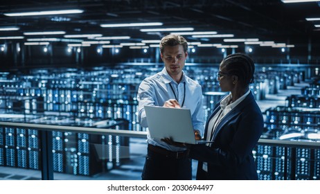 Data Center Female System Administrator and Male IT Specialist talk, Use Laptop. Information Technology Engineers work on Cyber Security Protection in Cloud Computing Server Farm. - Shutterstock ID 2030694497